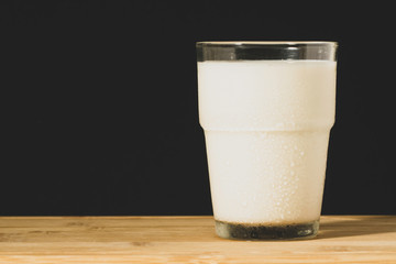 Glass of milk on a wooden surface and black background
