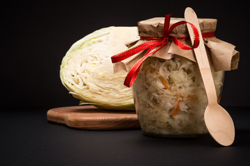 Fermented cabbage with herbs and spices in glass jar on the black background
