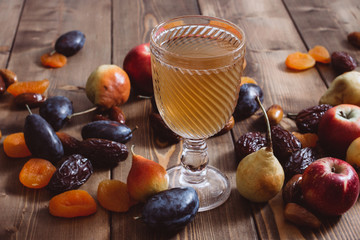 A glass cup with apricot apple plum pear fruit compote and ripe apricots on a wooden table. Sweet and healthy dessert.