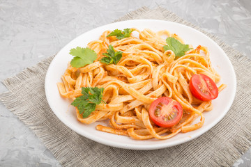 Semolina pasta with tomato pesto sauce, orange and herbs on a gray concrete background. Side view.