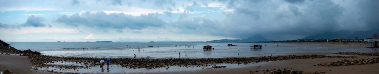 Ocean shore view at low tide on a rainy day, sand, water spills panorama. Travel by China and world
