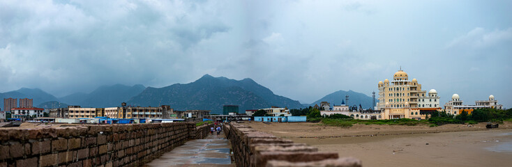 View to the old stone wall, to the village near the mountain in the seaside in China panorama. Morning sea rural landscape on a cloudy rainy day.
