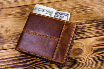 Brown leather wallet and one hundred dollar banknotes on the wooden background