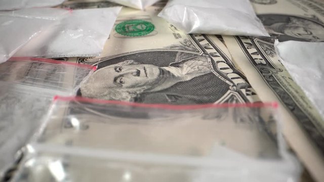 Dollar bills and white powder drugs in bags rotate in front of the camera
