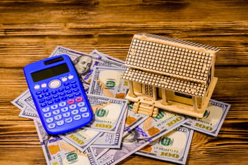 Plywood model of the house, calculator and one hundred dollar banknotes. Loan, real estate concept