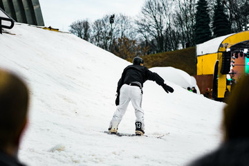 Man in a white pants and black jacket moving out from the slope on a snowboard. Snowboarder. Winter...