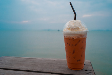 Ice Thai tea on the wooden table and the sea in the background.