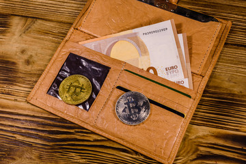 Brown leather wallet with fifty euro banknotes and bitcoins on the wooden background