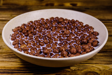 Ceramic plate with chocolate cereal balls in milk on wooden table