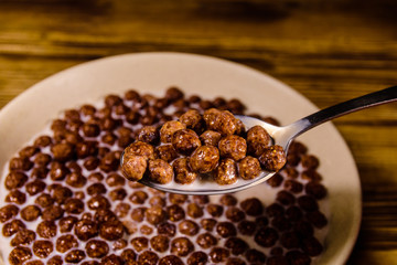 Ceramic plate with chocolate cereal balls in milk on wooden table