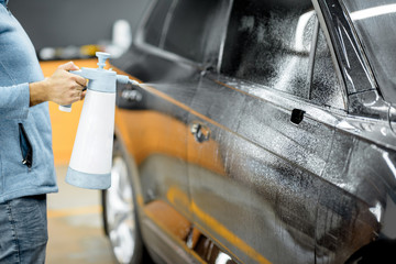 Car service worker splashing water on the car body, wetting it before anti-gravel film apply at the vehicle detailing service
