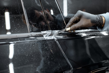 Worker trimming with cutter remains of a protective film, sticking it on a car body at the vehicle service
