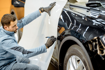 Man preparing protective film for sticking on a car body, marking it to with a pen at the vehicle...