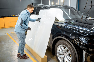 Fototapeta na wymiar Man preparing protective film for sticking on a car body, marking it to with a pen at the vehicle service station. Concept of car body protection with special films