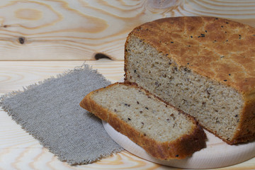 Freshly baked bread. A loaf of bread is cut and lies on a cutting board. Near a piece of linen fabric. Background from pine boards.