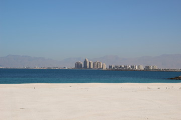 White sand beach and sea with far buildings and blue sky in Ras al khaimah