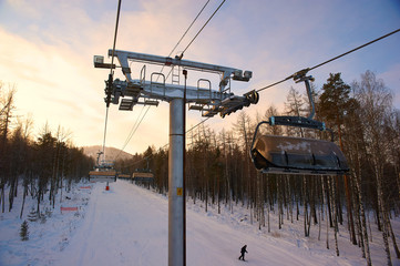 Cableway for skiers and snowboarders in the mountains covered by forest.