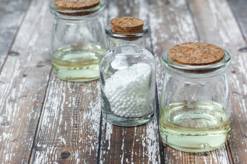 Classical Homeopathy globules lie on the leaves and vintage glass bottles on white background. Alternative Homeopathy medicine herbs, healtcare and pills concept. Place for text.