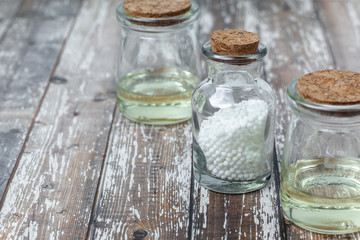 Classical Homeopathy globules lie on the leaves and vintage glass bottles on white background. Alternative Homeopathy medicine herbs, healtcare and pills concept. Place for text.