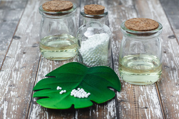 Classical Homeopathy globules lie on the leaves and vintage glass bottles on white background. Alternative Homeopathy medicine herbs, healtcare and pills concept. Place for text.