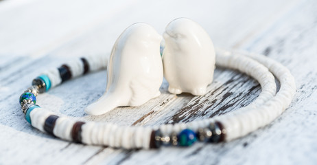 Rustic sea souvenirs from summer holiday background. Two love birds - lovely couple of porcelain sparrows kissing each other in white shell pieces and turquoise blue gemstone necklace circle.