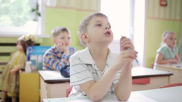 A boy holds a pencil in his mouth, thinking with a pencil in his mouth. A young boy holds a pencil in his mouth and solves the task.