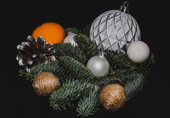 Art installation on a black background for New Year or Christmas from spruce twigs, glass balls, cord-balls, pine cone and mandarin in the hard light.