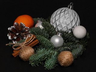 Art installation on a black background for New Year or Christmas from spruce twigs, glass balls, cord balls, pine cone, one mandarin and cinnamon sticks.