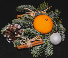 Art installation on a black background for New Year or Christmas from spruce twigs, one glass ball,  pine cone, one mandarin and cinnamon sticks.