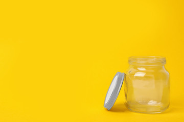 Open empty glass jar on yellow background, space for text