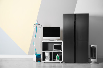 Modern refrigerator and other household appliances near color wall indoors