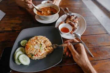 Traditional Thai Food: White Man and Girl Eat Fried Rice with Shrimp, Tom Yam and Grilled Chicken. Asian travel.