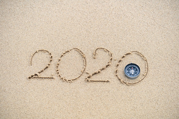 Fototapeta na wymiar Compass and 2020 message written in the sand at the beach background. concept for vision 2020.