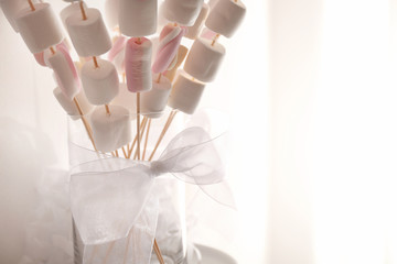 Tasty marshmallow on wooden sticks with bow for birthday party on blurred background, closeup