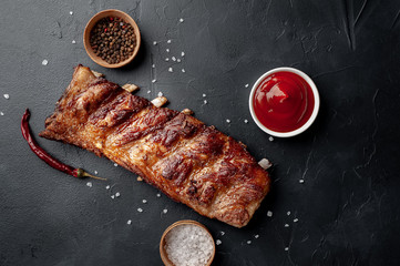 grilled pork ribs with spices and ketchup on a stone background