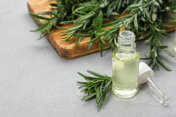 Fresh rosemary and bottle of essential oil on light grey table. Space or text