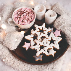 Ginger breads in star shape with coffee cup ovr glowing lights on knitted sweater closeup. Xmas. Good morning.