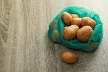 Net bag with potatoes on wooden table. Space for text