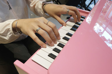 Close up the hands of a young woman playing pink tiny piano, with Selective focus