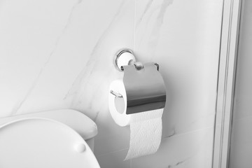 Holder with toilet paper roll on wall in bathroom