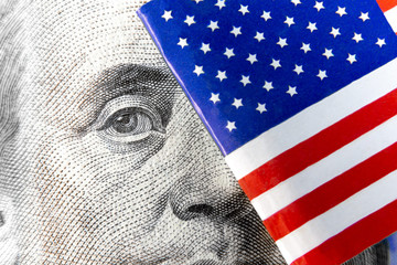 Extreme macro of Benjamin Franklin from one hundred dollar banknote hiding out behind micro flag of...