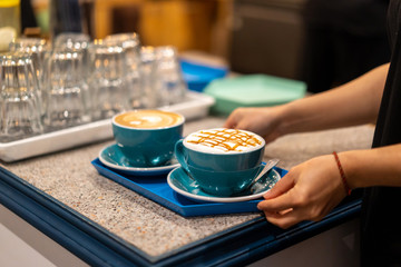 Delicious coffee in blue mugs on a tray in a cafe served by a waiter.