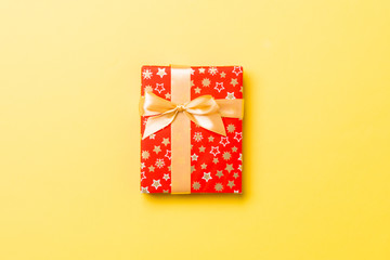 Top view Christmas present box with gold bow on yellow background with copy space