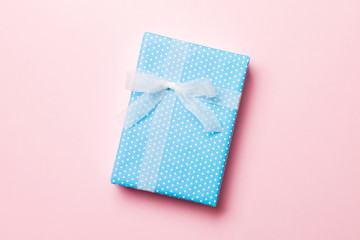 Gift box with white bow in hands for Christmas or New Year day on pink background, top view with copy space
