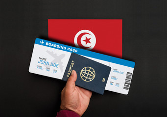 Hand holds passport and boarding pass with flag of Tunisia