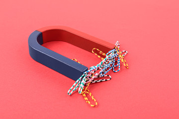 Magnet attracting paper clips on red background