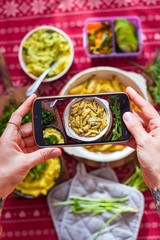 Taking food photo on phone screen in cafe or restaurant. Smartphone photography of vegan food - potato and vegetables. Woman hands