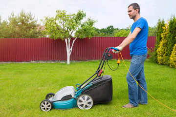 Fototapeta premium Worker with a lawn mower mows grass in the garden. Side view.