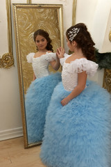 girl young princess in white with a blue dress and hairpin in black hair curls at the mirror in a...