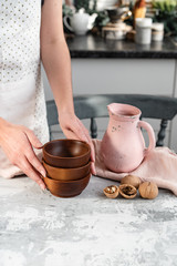 Woman's hands in an apron put on the kitchen table with a jug a stack of wooden plates